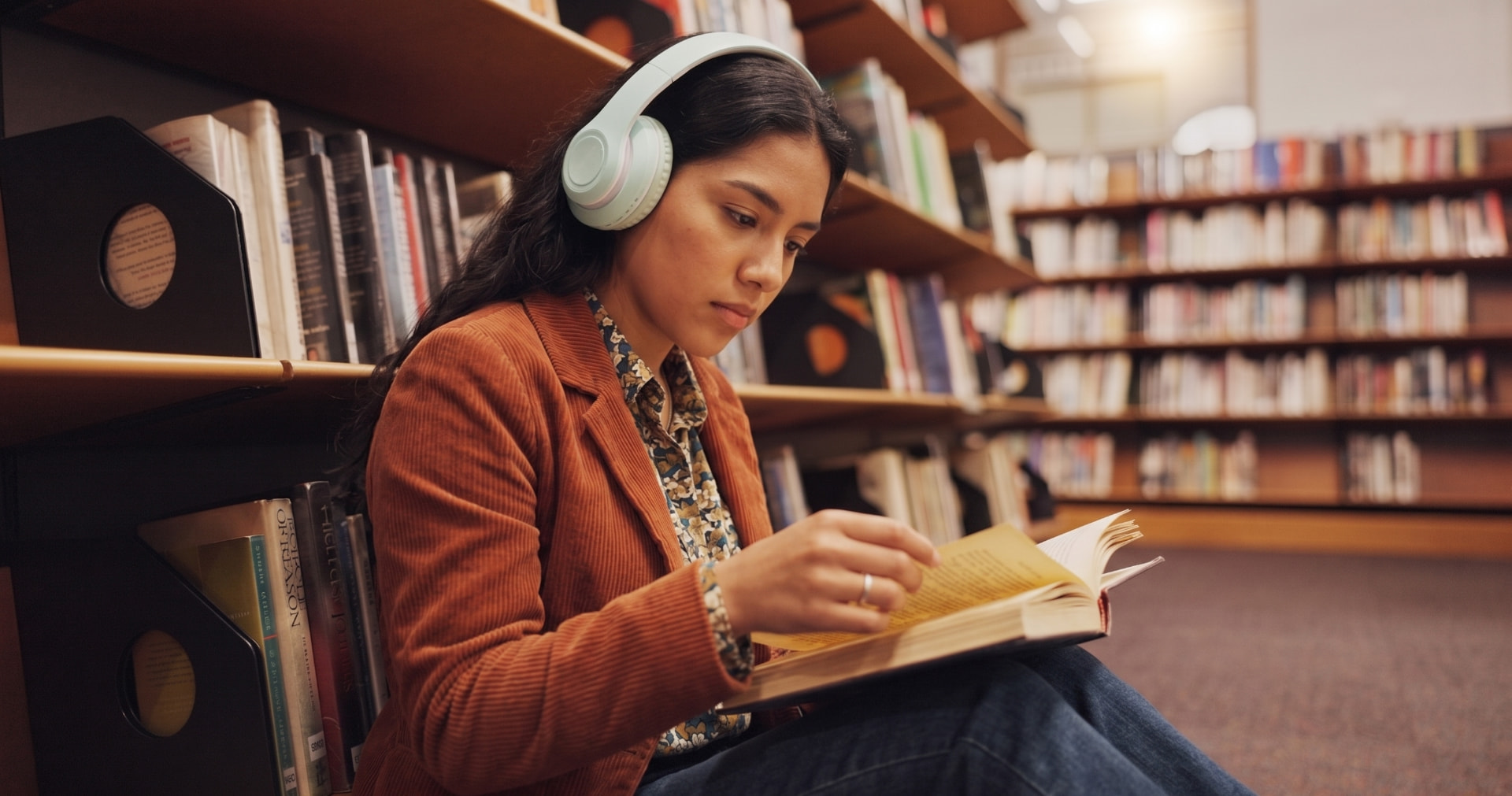 Estudiante leyendo en una biblioteca con audífonos